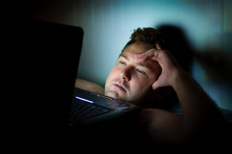 man lying on bed with laptop on top of chest watching something