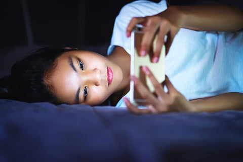 teen girl lying in bed at night and using smart phone